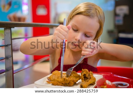 Adorable girl have meal with chicken,  soda drink and fried potatoes at fast food restaurant