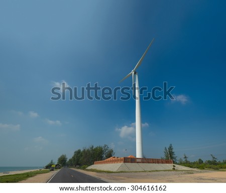 White wind turbine generating electricity on the ocean beach with blue sky
