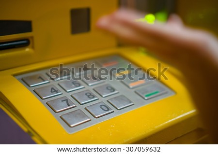Close up of ATM keypad and hand on keys with withdrawal and card holes light on