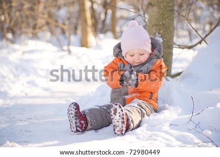 Adorable baby sit on snow road and play with snow in park