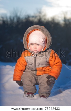 Adorable serious baby squat on top of hill in park with sun on back