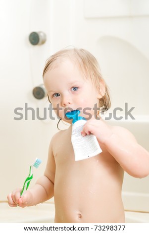 Adorable baby brushing teeth in shower holding tooth paste