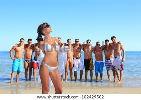 Group of eleven handsome guys on the beach looking at a beautiful girl in bikini