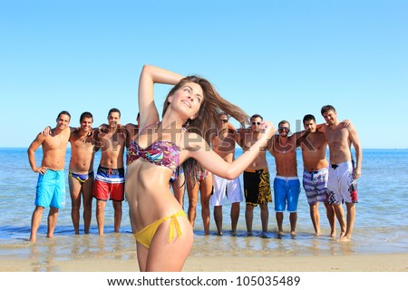 Group of eleven handsome guys on the beach looking at a beautiful girl in bikini