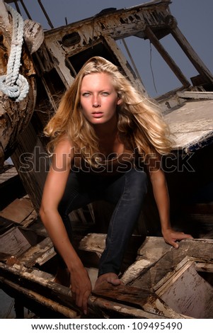 portrait of sexy blond woman in jeans posing in from of shipwreck
