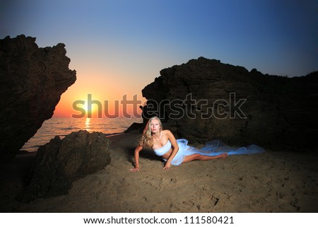 Beautiful young woman on the beach wrapped in white wedding veil at sunrise