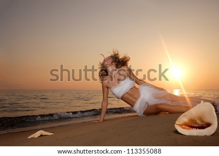 Beautiful young woman on the beach wrapped in white wedding veil at sunrise
