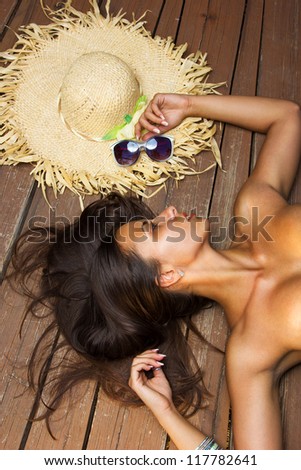Sexy fit bikini model with hat and sunglasses posing on wooden floor