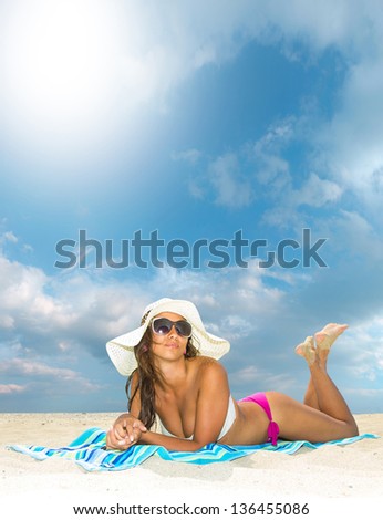 Beautiful young woman in bikini with straw hat laying on the beach