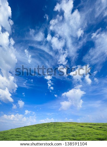 Green grass hills under midday sun in blue sky.