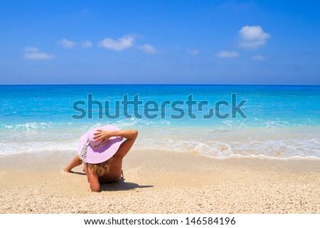 Woman laying on the beach in beach pink straw hat enjoying summer holidays looking at the ocean