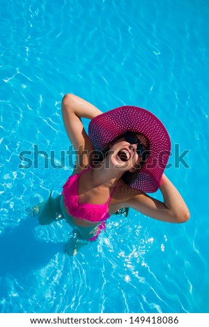 Young woman in bikini wearing a straw hat in the swimming pool making faces