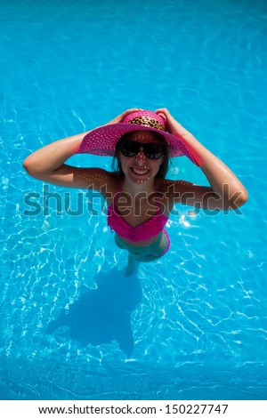 Young woman in bikini wearing a straw hat in the swimming pool making faces