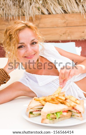 Beautiful young woman at the summer lounge eating a club sandwich