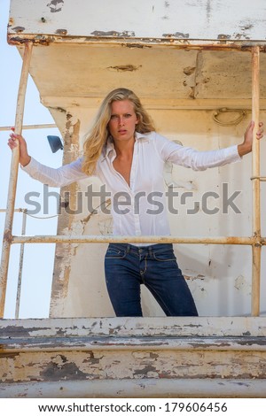 Young blonde woman in blue jeans  posing at shipwreck