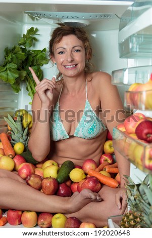 Woman sitting in a fridge in the lotus position surrounded by fruits making faces