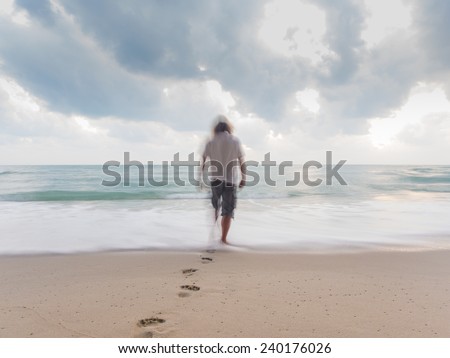 Back view of a man walking and leaving footprints on the sand of a beach - Motion blur