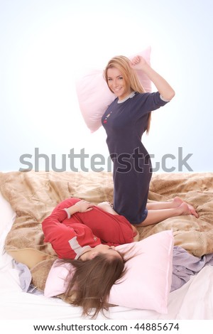 Two beautiful young woman fighting with pillows in bed