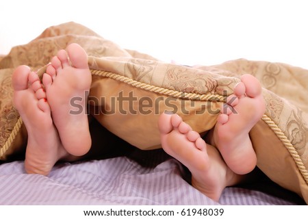 View of a couple's feet sticking out of the bed sheet while in bed