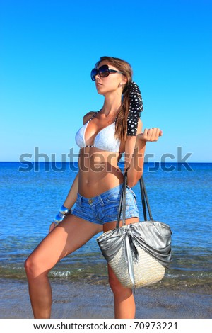 Beautiful young woman holding her bag relaxing on the beach in Greece