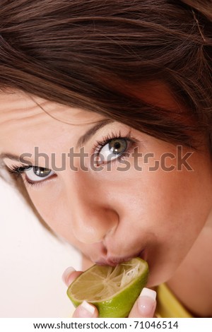 A woman taking a bite out of a lime. The sour flavor of the lime made her make a funny face.