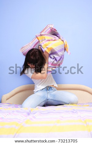 Woman having pillow fight in bed with motion blur