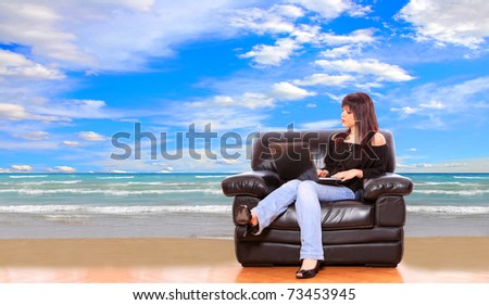 Young woman sitting on couch on the beach checking her vacation on her laptop - travel concept