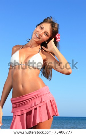 Young beautiful fit woman with bikini top and pink skirt  posing at the beach