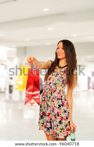 lovely brunette woman in light dress with colorful shopping bags at the mall