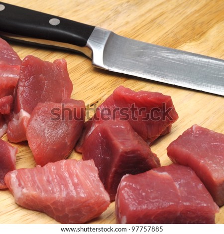 fresh uncooked beef meat sliced in cubes on board with carving knife