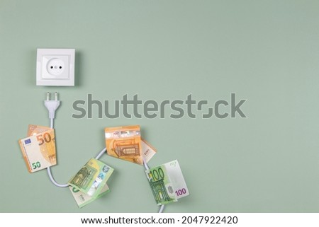 Electric power plug with euro banknotes on it and electric socket on light green background. Electricity cost and expensive energy concept