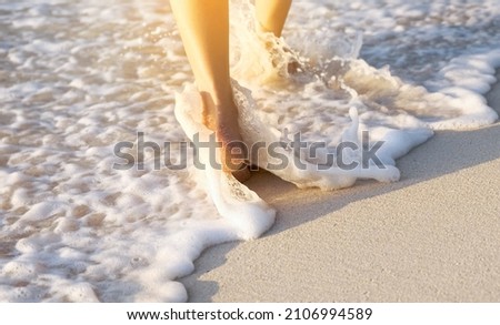woman walking to sea and beach on a beautiful island Ocean foam wrapped around a girl's leg. Her legs touched the splashing water. Hit the skin on the legs and she walked in the soft sunshine in the m Stock fotó © 