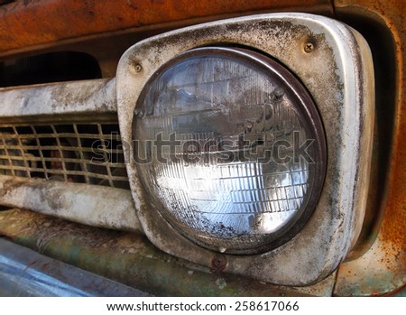 Closeup of headlight on the grill of a rusting vintage truck.