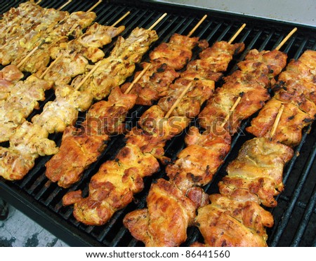 Pieces of chicken on bamboo skewers cooking over a hot charcoal grill.