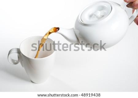 Cup of tea being poured from white ceramic teapot