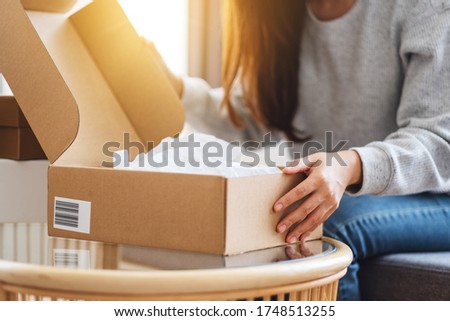 Close up image of a woman receiving and opening a postal parcel box at home for delivery and online shopping concept
