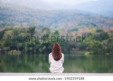 Rear view image of a woman sitting alone by the lake looking at the mountains with green nature background Stock foto © 