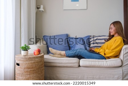 A beautiful young asian woman using and working on laptop computer while laying down on a sofa at home Foto stock © 