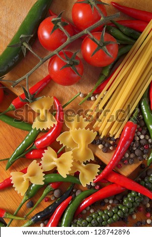 different types of hot peppers cherry tomatoes and pasta on a wooden cutting board