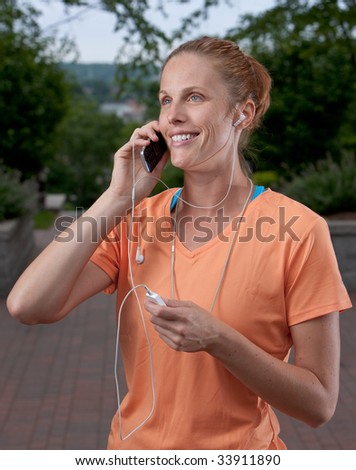 Woman pauses from jogging to talk on a cell phone and listens to an mp3 player