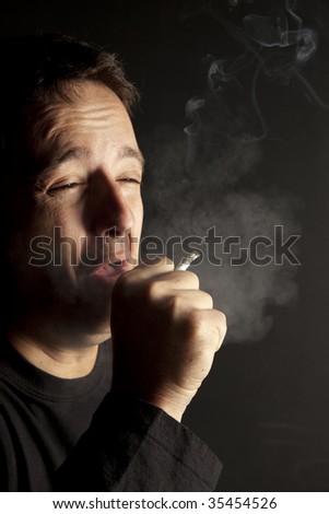 Man coughing out cigarette smoke holding a cigarette in his hand.