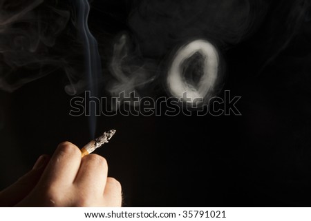 Hand holding cigarette with smoke ring on black background