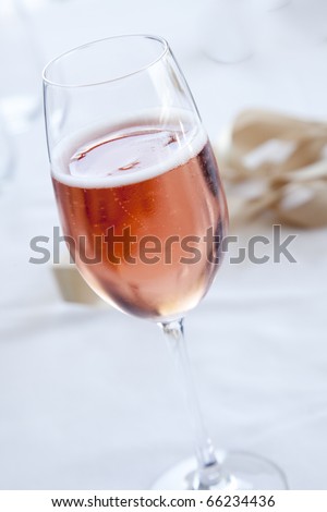 Pink sparkling wine on a white cloth in champagne flute with a ribbon in the background.
