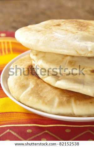 Pita bread on a plate on a red, yellow and orange fabric.