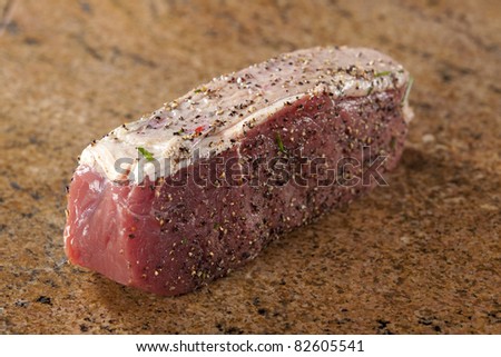 Spiced fillet cutlet on brown granite cutting board.