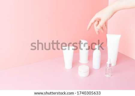 Skincare routine- Women hand choosing skin care products for healthy skin on pink background. Packaging of facial foam, cleansing, essence, serum, cream/lotion. Beauty and cosmetic concept. Minimal.