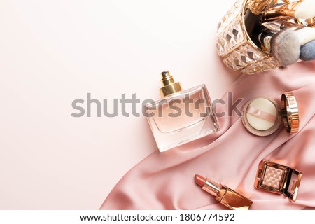 Perfume bottle with makeup cosmetics on pink silk folded fabric background. Scent fragrance cosmetic beauty product. Flat lay.