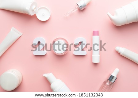 Best skincare products and cosmetic trends of 2021 concept. 2021 white number with lip balm, cream bottle, serum and lotion on pink background.