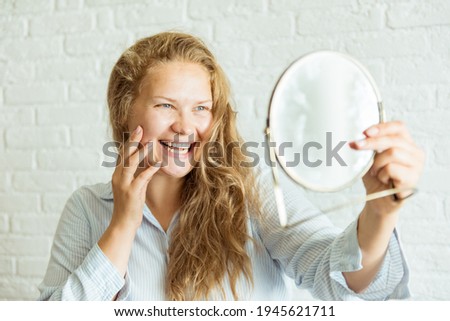 Happy woman applying cream and looking at mirror over grey background. Concept about body positivity, self esteem, and body acceptance 商業照片 © 
