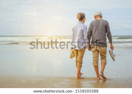 Senior couple walking on the beach holding hands at sunrise, plan life insurance at retirement concept. Imagine de stoc © 